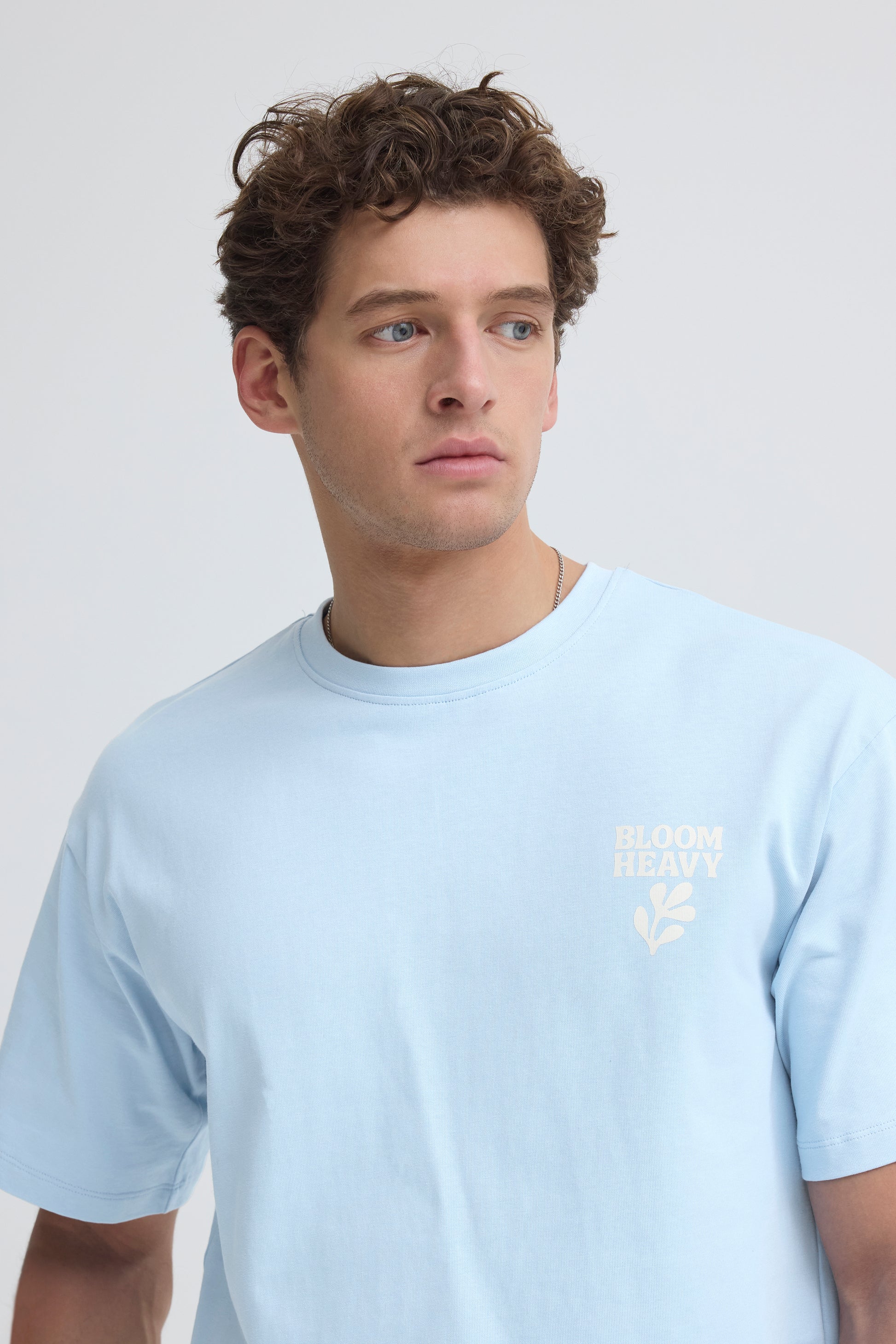 Man wearing a light blue t-shirt with a logo on a plain background