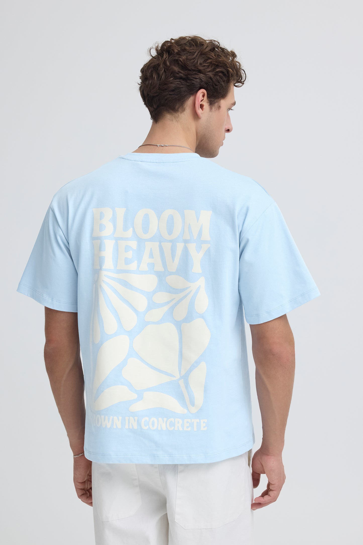 Person wearing a light blue t-shirt with 'BLOOM' text and leaf design on the back, standing against a plain background.