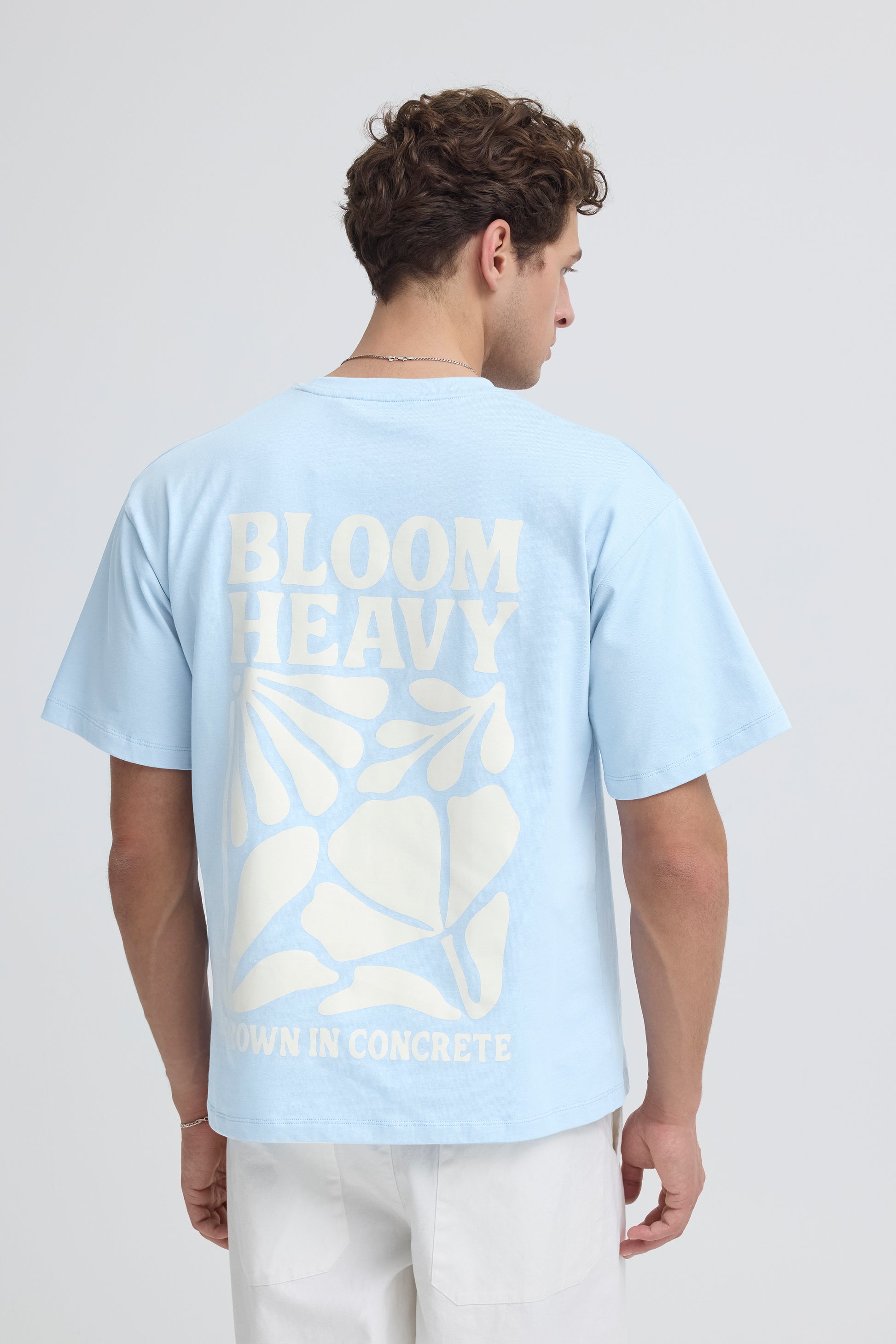 Person wearing a light blue t-shirt with 'BLOOM' text and leaf design on the back, standing against a plain background.