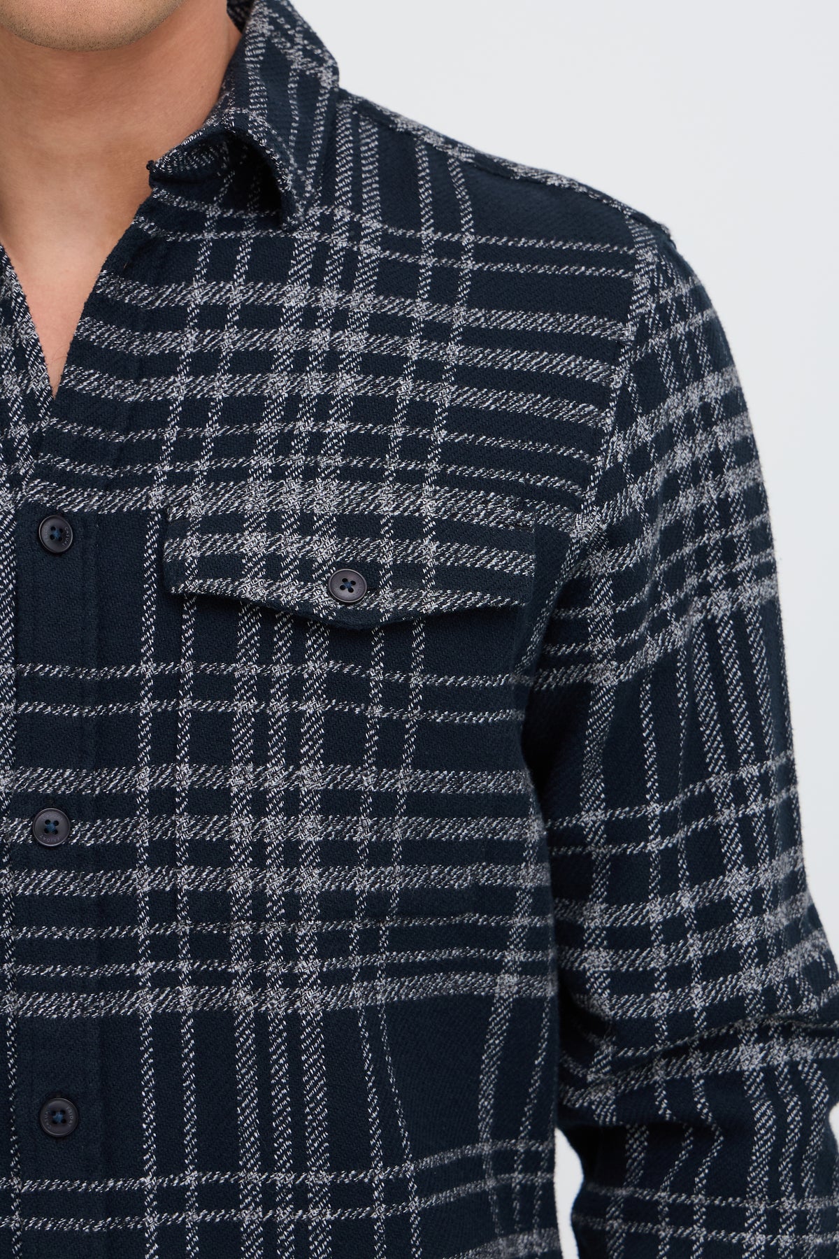 Close-up of a man wearing a dark navy and gray plaid flannel shirt, showing the chest pocket and buttons.