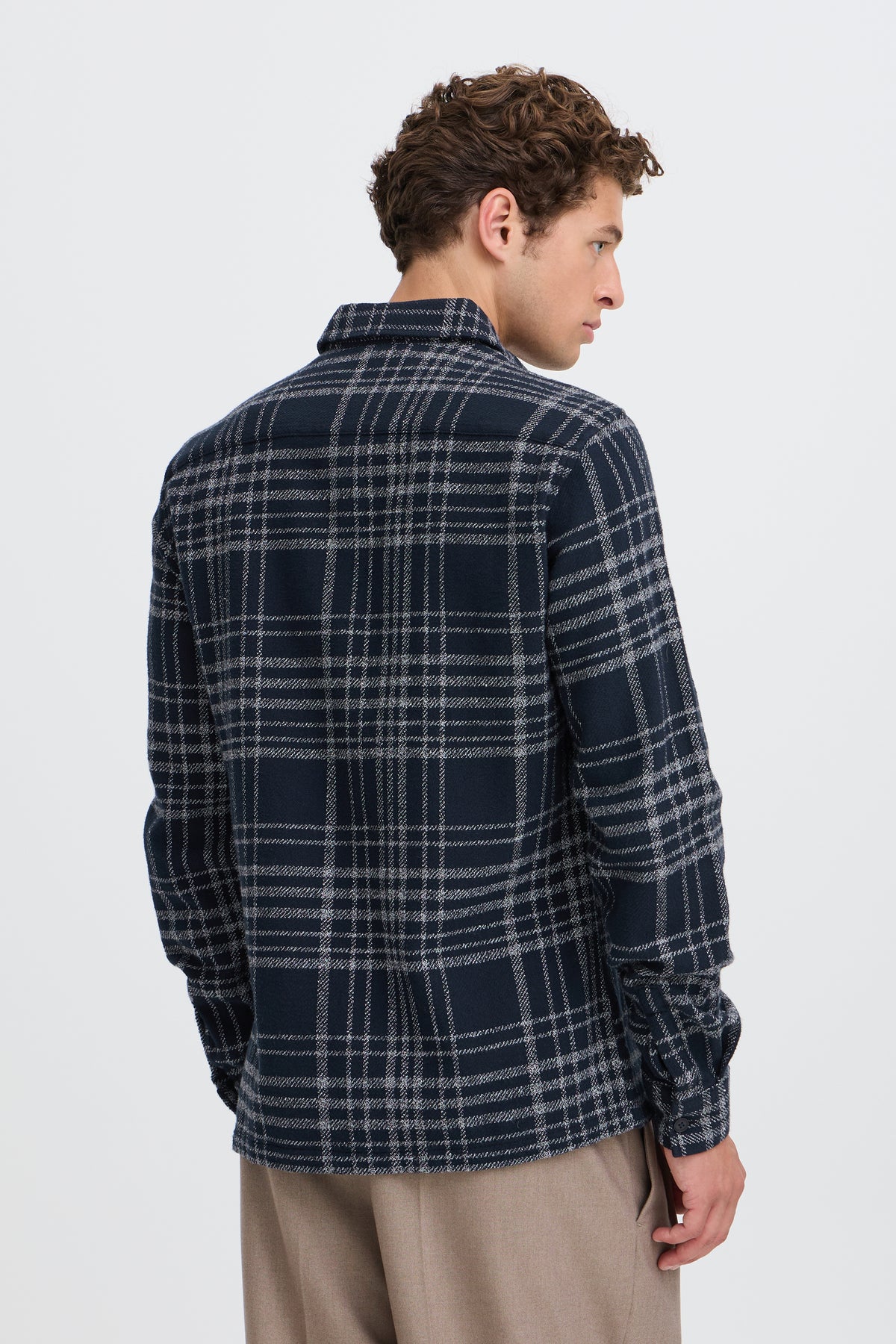 A man wearing a navy blue and gray plaid flannel shirt, shown from the back against a light gray studio background.