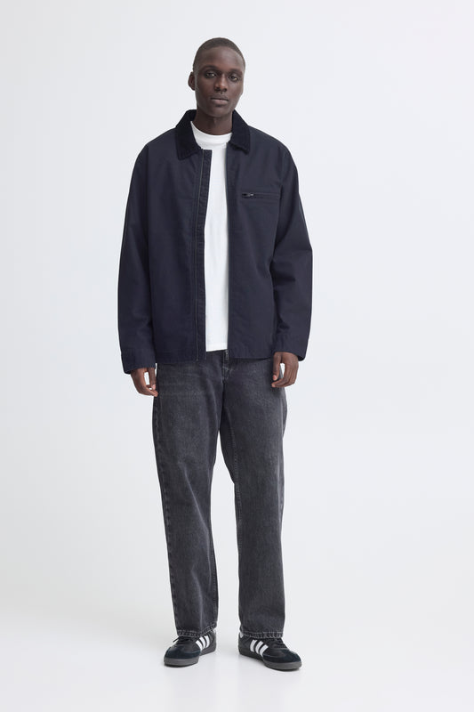 Man wearing a dark jacket, white shirt, gray jeans, and black shoes on a white background