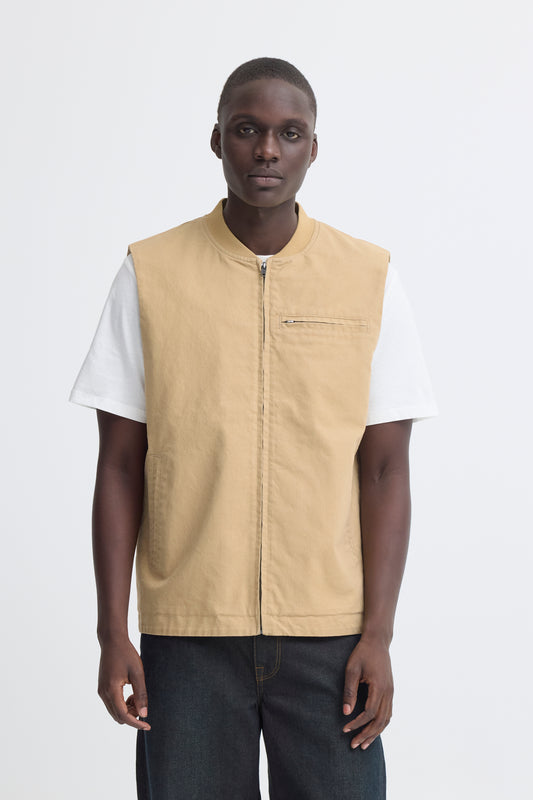 Man wearing a beige vest over a white shirt on a white background