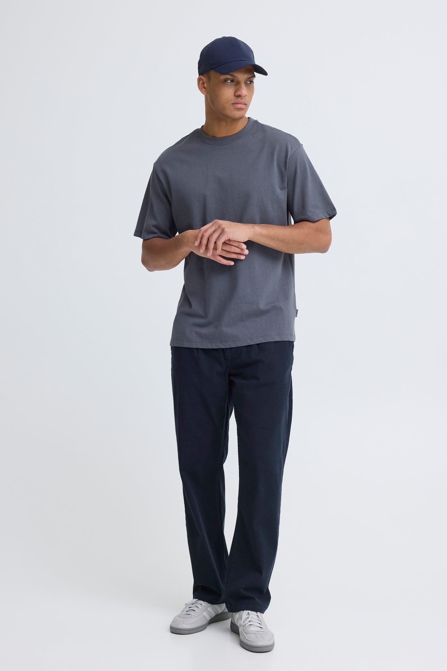 Person wearing a gray t-shirt, navy cap, and dark pants on a white background