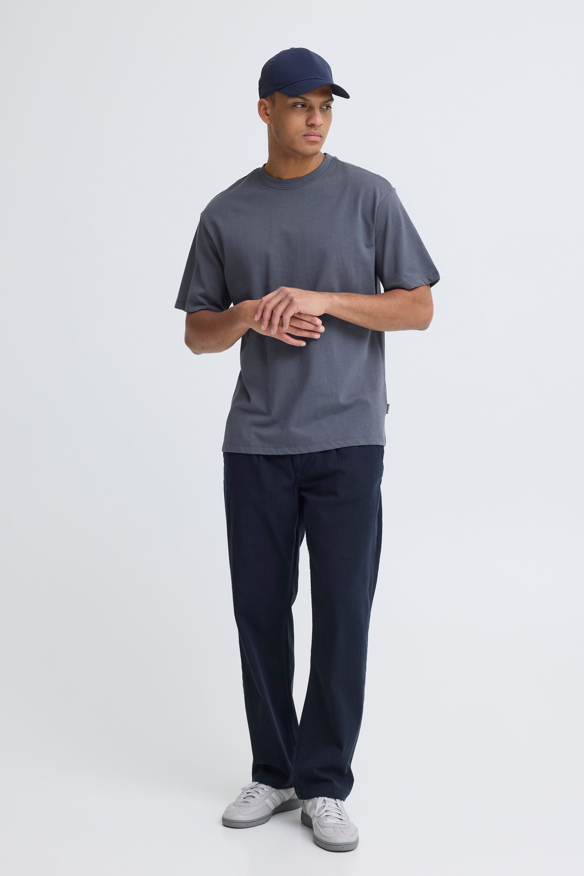 Person wearing a gray t-shirt, navy cap, and dark pants on a white background