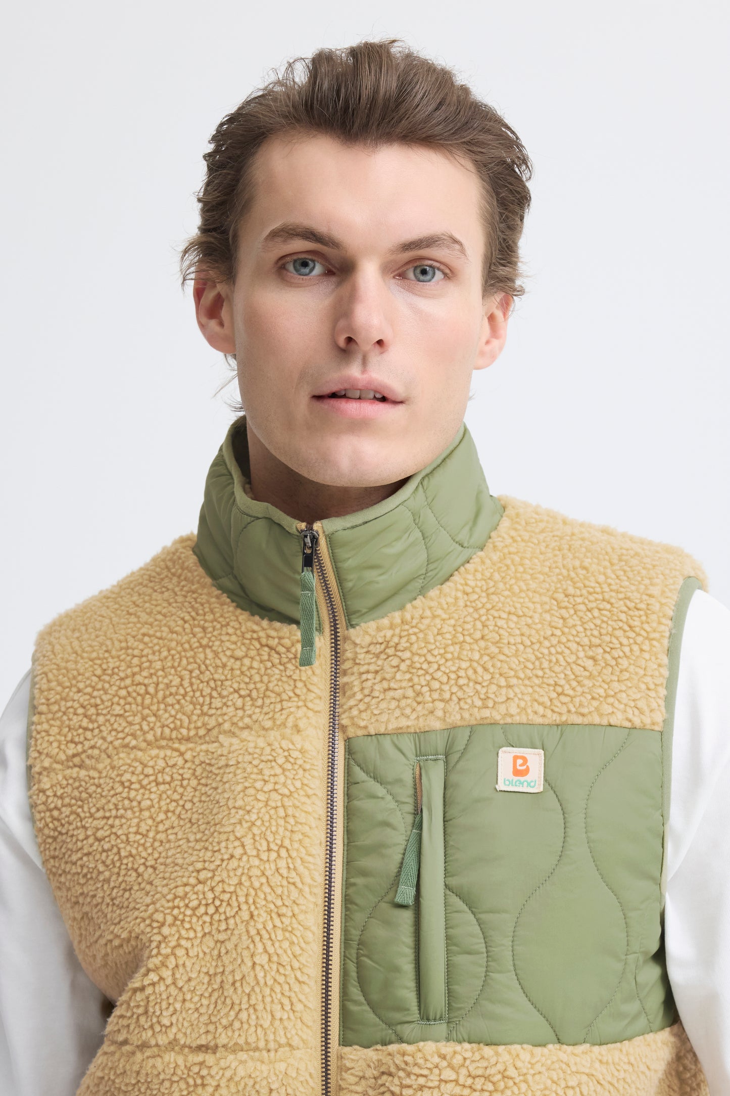 Man wearing a beige and green Carhartt vest on a white background