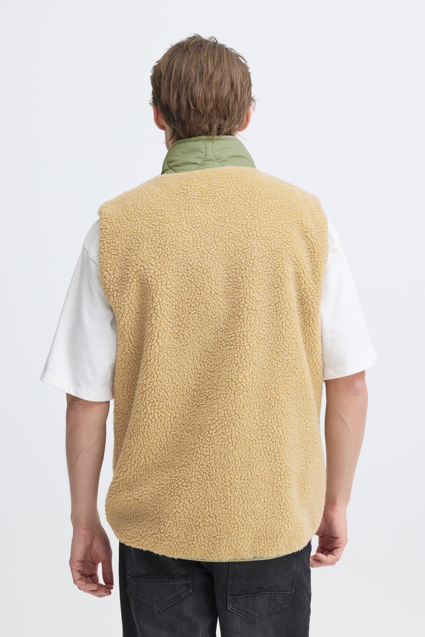 Person wearing a beige fleece vest over a white shirt on a white background