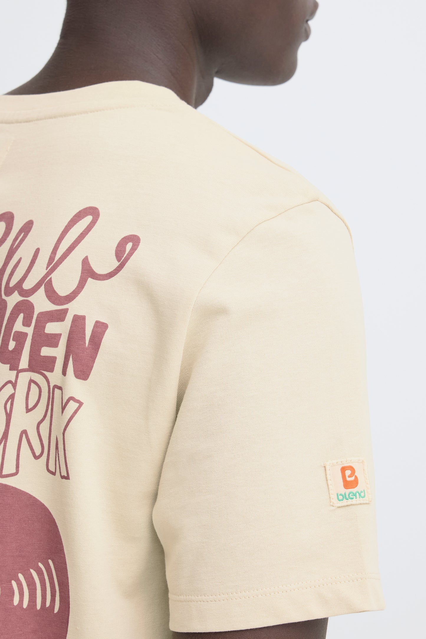 Beige t-shirt with graphic design and brand logo on a plain background