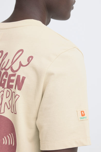 Beige t-shirt with graphic design and brand logo on a plain background