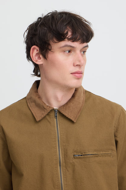 A close-up shot of a man wearing a brown corduroy collar jacket with a front zipper and a zippered chest pocket, set against a plain light gray background.