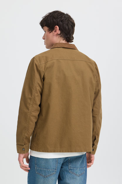 A man shown from the back wearing a brown utility jacket over a white t-shirt and blue jeans, photographed against a light gray studio background.