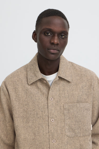 A man wearing a light beige textured overshirt with a collar and front buttons over a white t-shirt, photographed against a neutral light gray background.