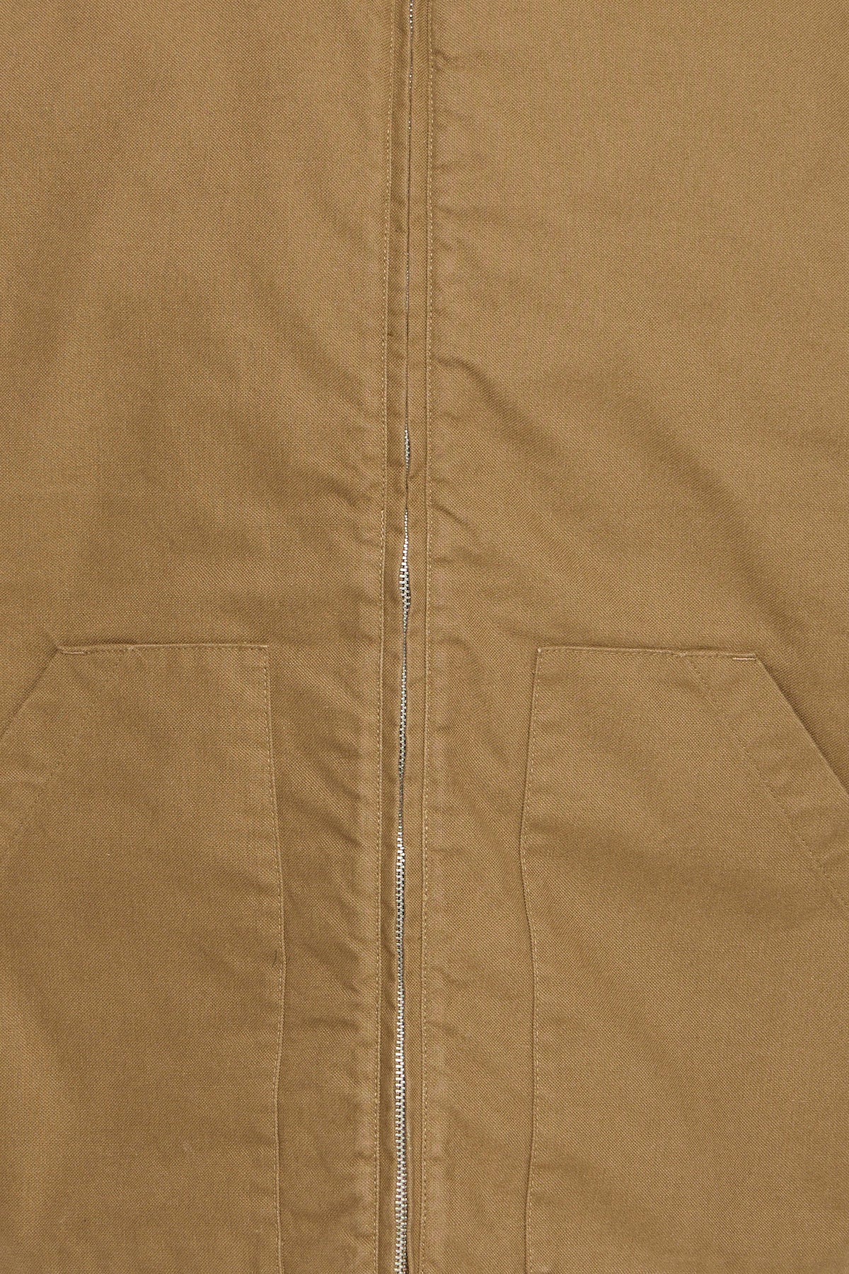 Close-up of a tan or camel-colored jacket or overshirt with a front zipper and two large patch pockets.