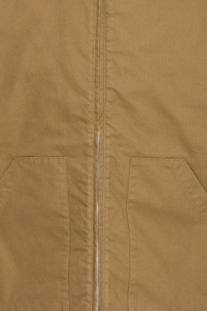 Close-up of a tan or camel-colored jacket or overshirt with a front zipper and two large patch pockets.