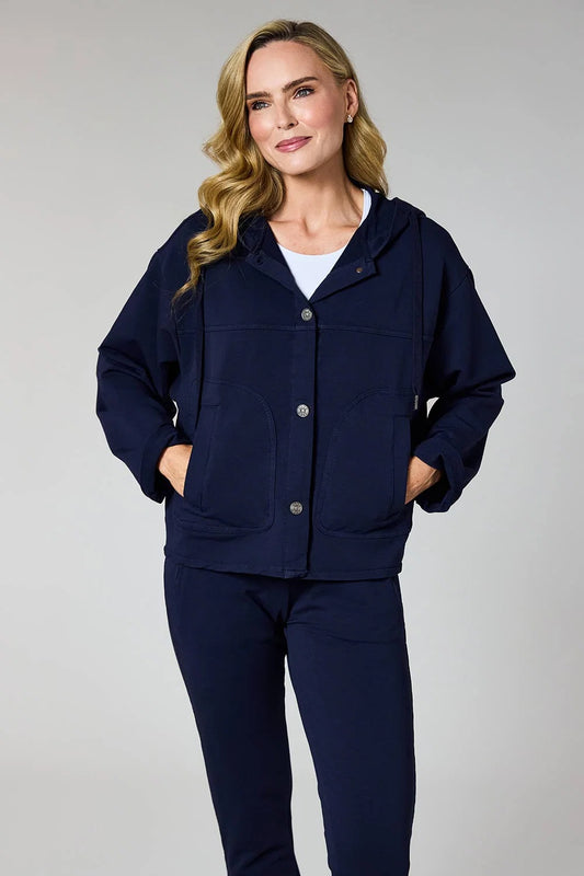A woman modeling a navy blue hooded jacket with a button front and large front pockets, paired with matching navy pants, against a light gray studio background.