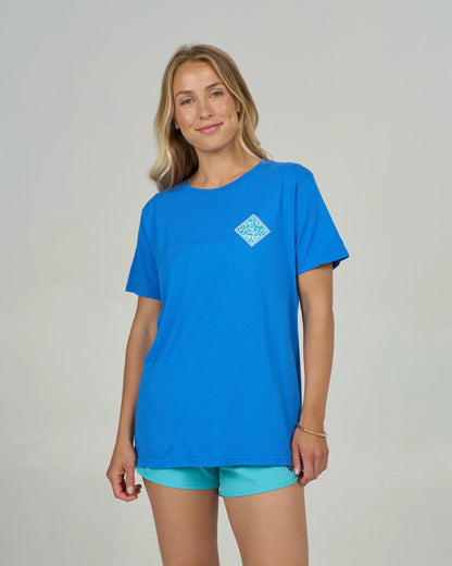 Woman wearing a blue t-shirt with a logo and turquoise shorts on a gray background