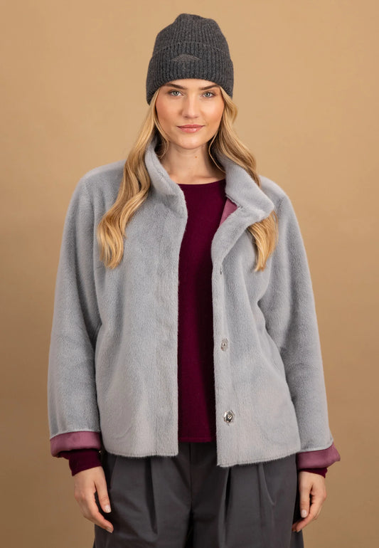 Woman wearing a gray coat, maroon shirt, and dark beanie against a brown background