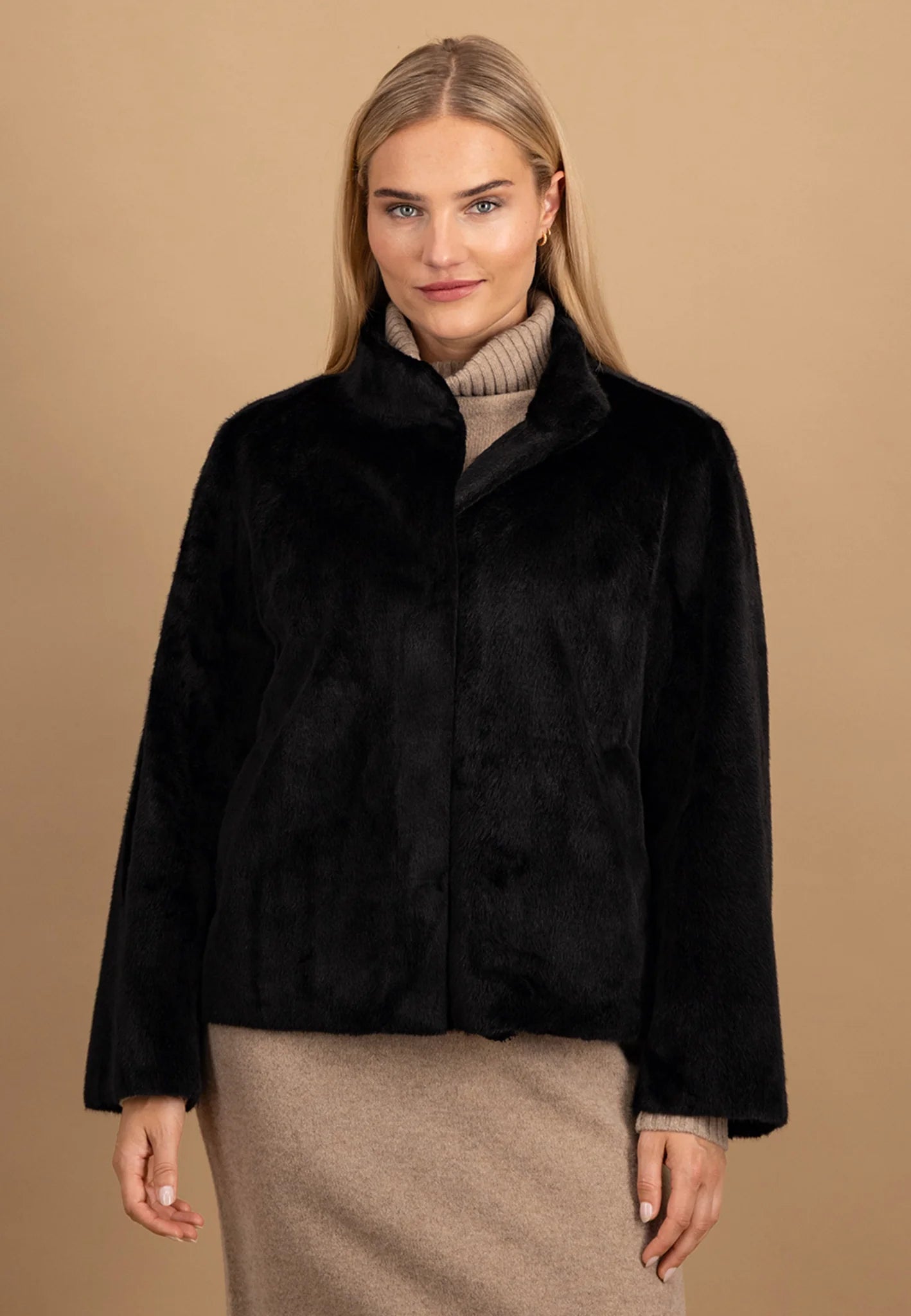 Woman wearing a black fur coat against a beige background