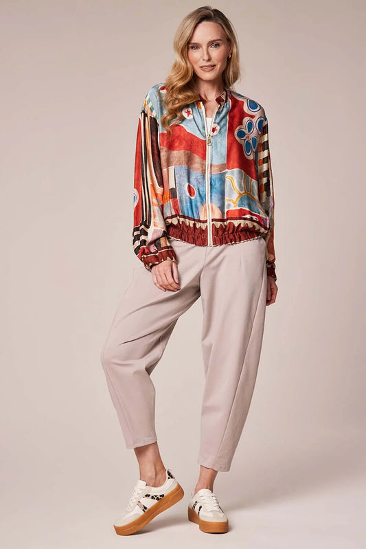 Person wearing a colorful jacket, light gray pants, and white sneakers on a plain background