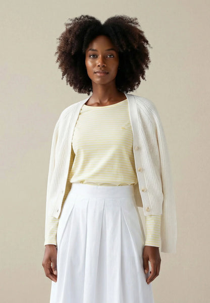 Woman wearing a light yellow top and white skirt with a beige cardigan against a beige background