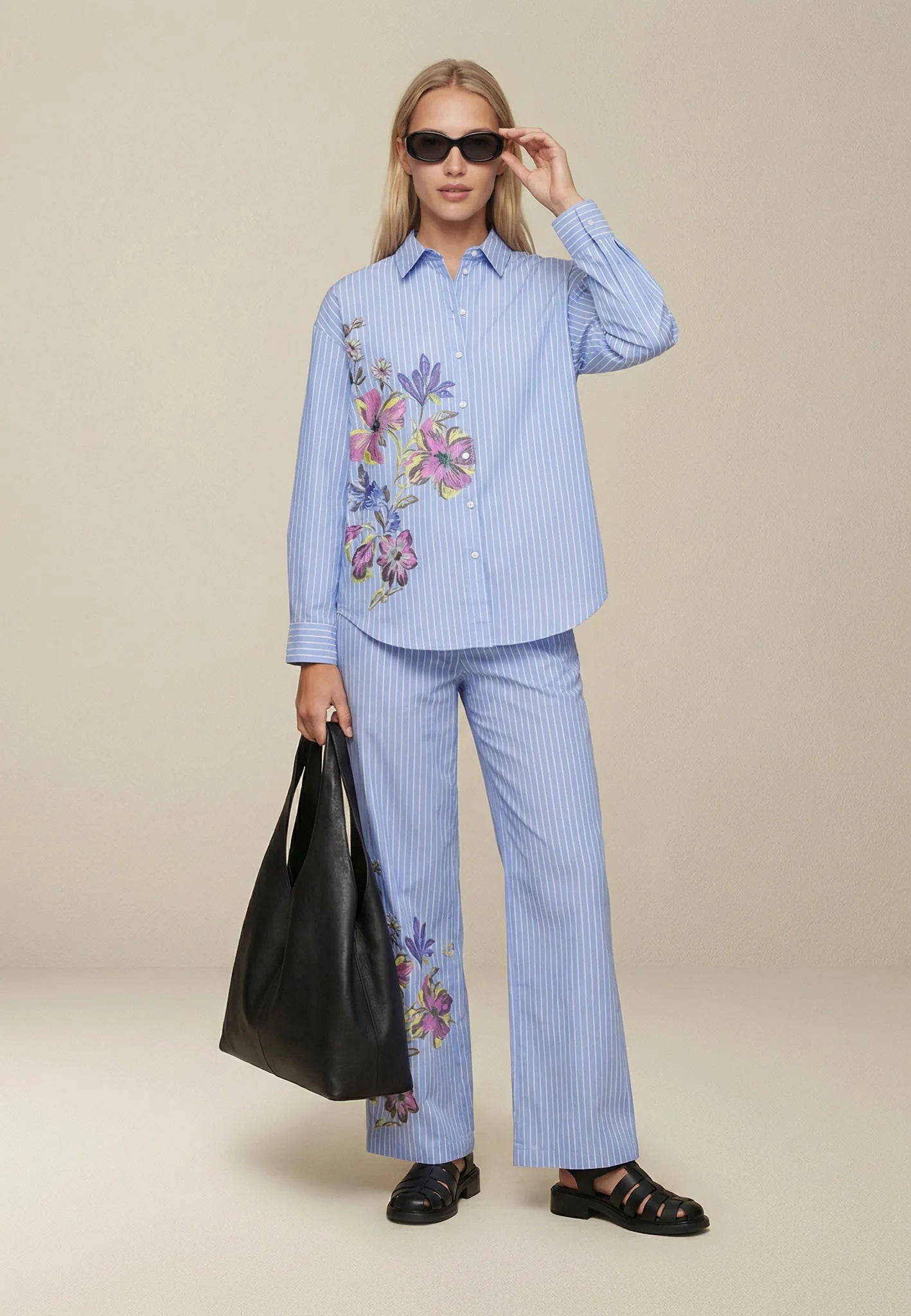 Woman wearing a blue striped outfit with floral embroidery, holding a black bag.