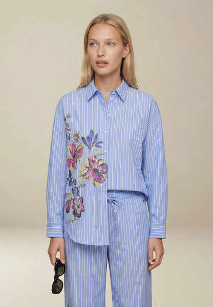 Woman wearing a blue striped shirt with floral embroidery and matching pants on a beige background