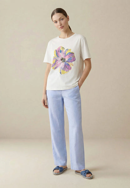 Woman wearing a white t-shirt with a colorful flower design and light blue pants on a beige background