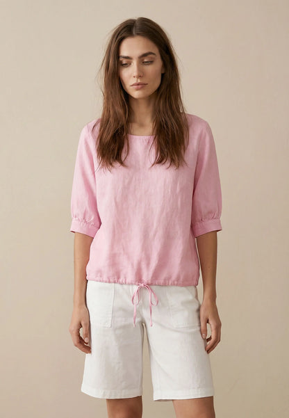 Woman wearing a pink top and white shorts against a beige background