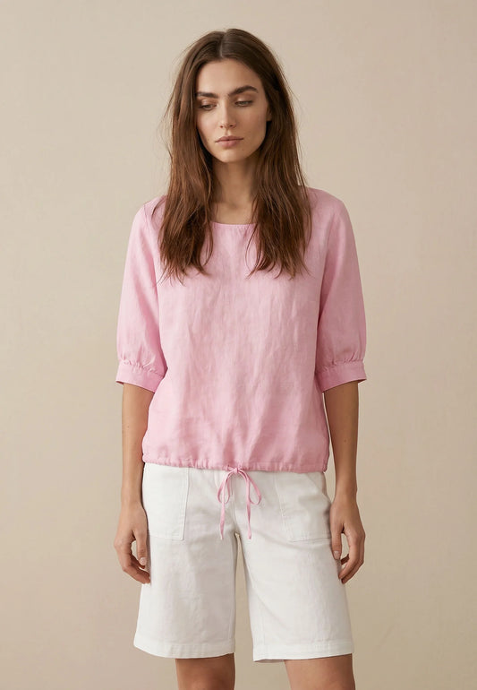 Woman wearing a pink top and white shorts against a beige background