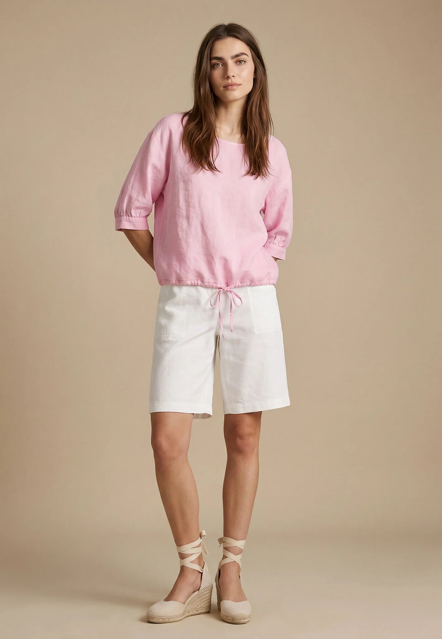 Woman wearing a pink top and white shorts against a beige background