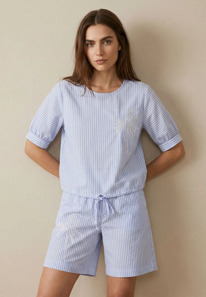 Woman wearing a blue and white striped pajama set against a beige background