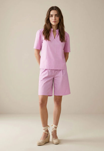 Woman wearing a pink outfit with shorts on a beige background