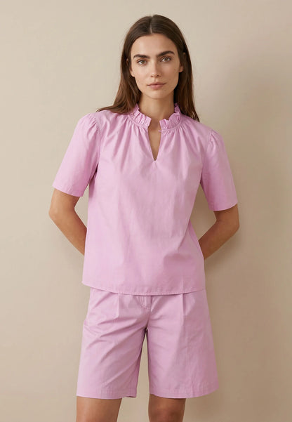 Woman wearing a pink outfit with a top and shorts against a beige background