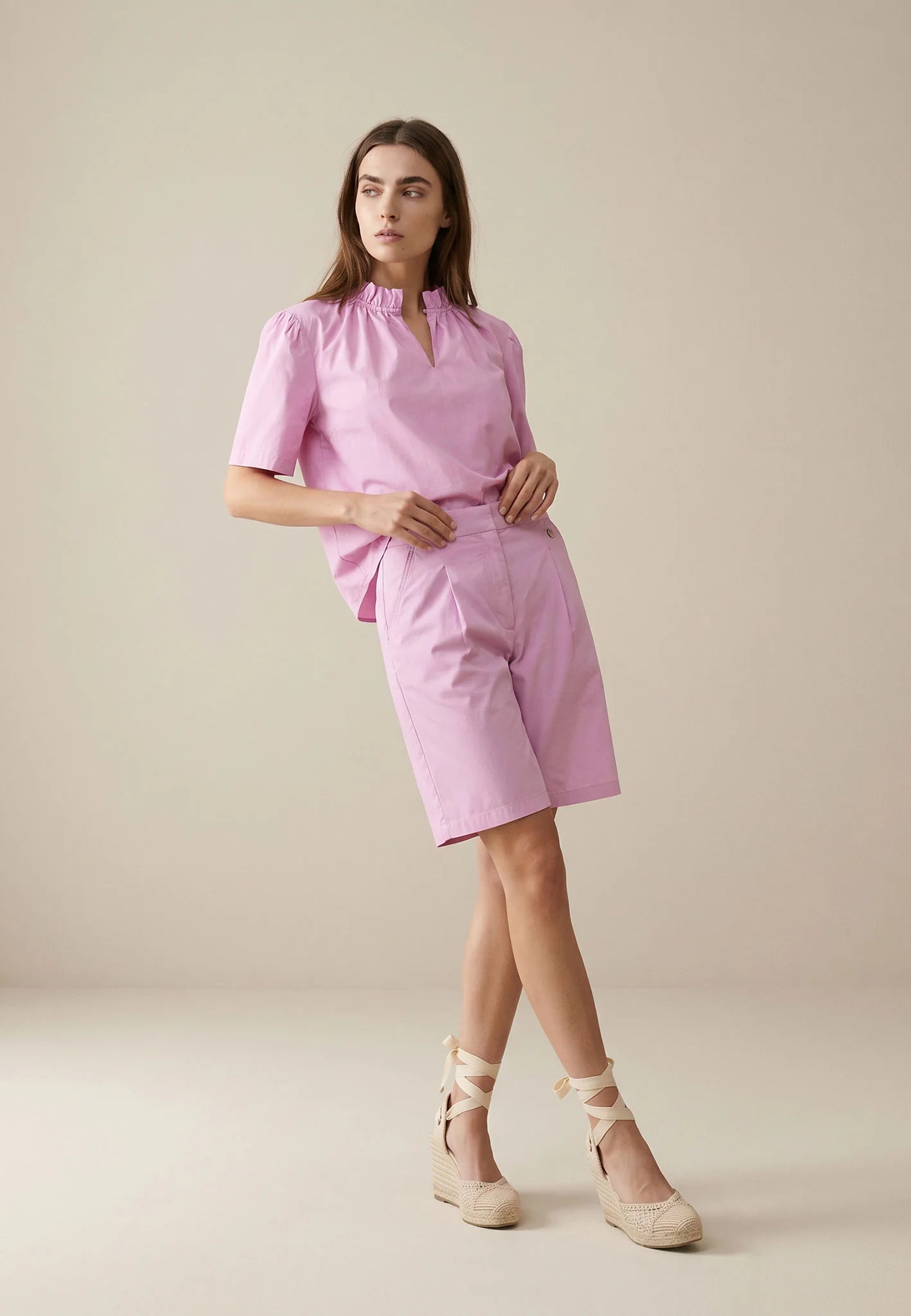 Woman wearing a pink outfit with a top and shorts on a beige background