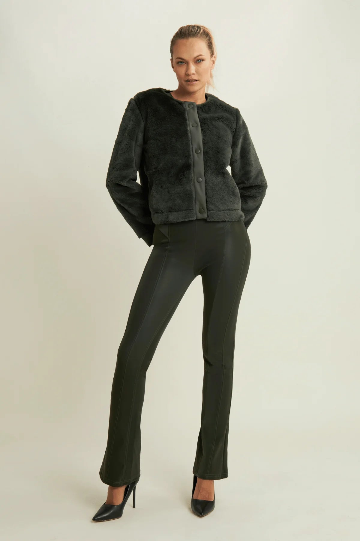 Woman wearing a dark green jacket and pants on a plain background