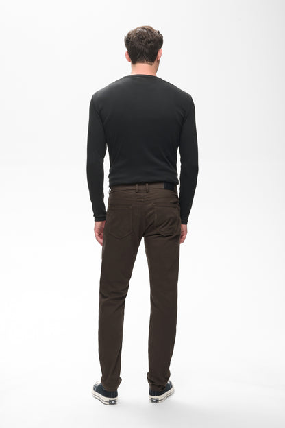 A man viewed from behind wearing a black long-sleeve crewneck shirt and dark brown trousers, standing against a plain white studio background.