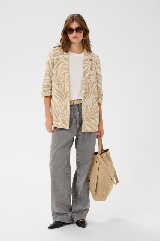 Woman wearing a patterned beige jacket, white shirt, gray pants, and black shoes, holding a beige bag on a white background.