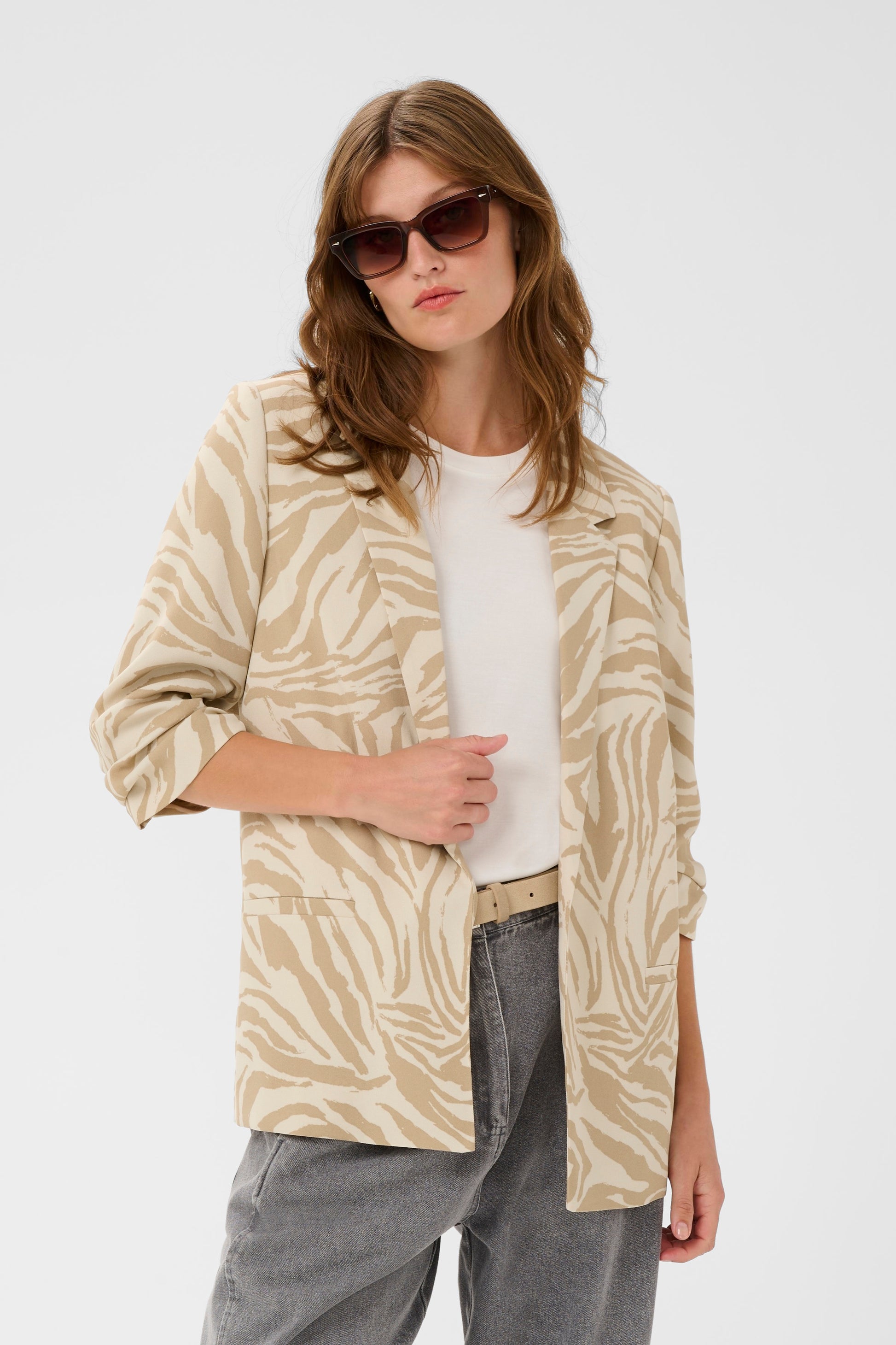 Woman wearing a beige patterned cardigan over a white shirt and gray pants on a white background