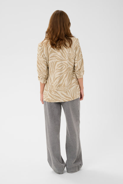 Woman wearing a patterned beige shirt and gray pants on a white background