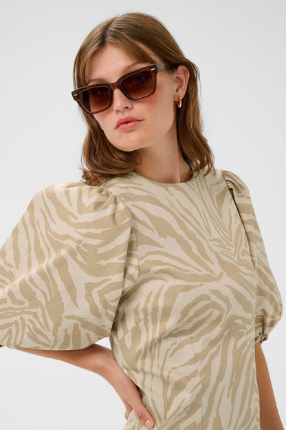 Woman wearing a beige patterned dress and sunglasses on a white background