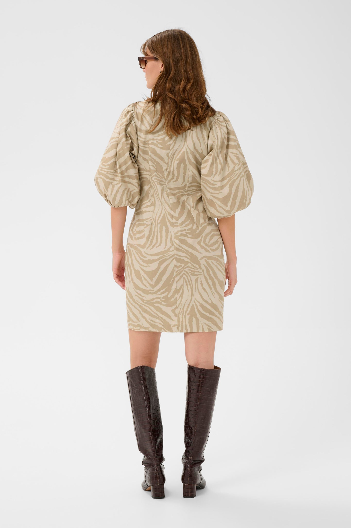 Woman wearing a patterned dress and knee-high boots on a white background