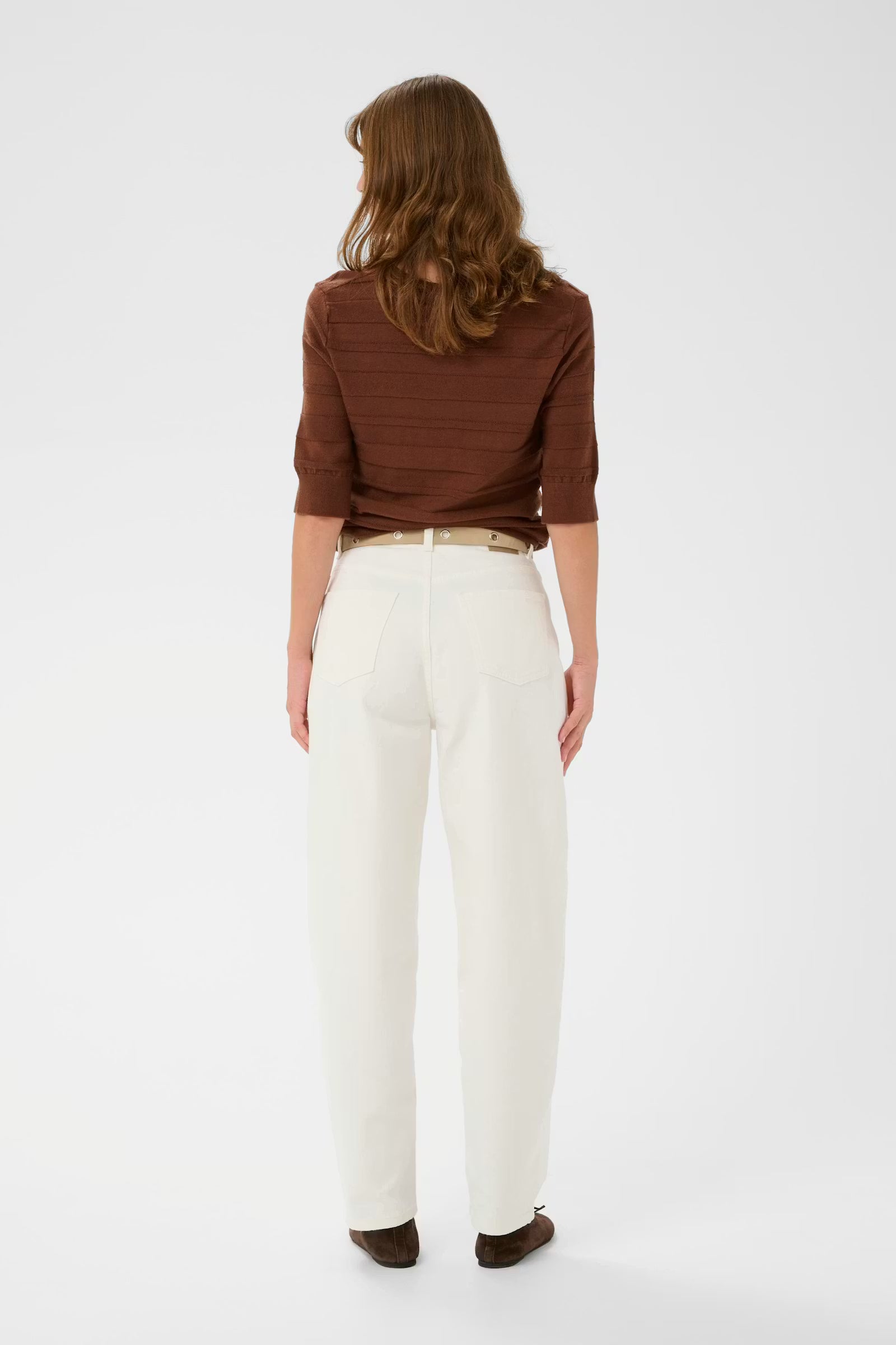 Woman wearing a brown top and white pants on a white background