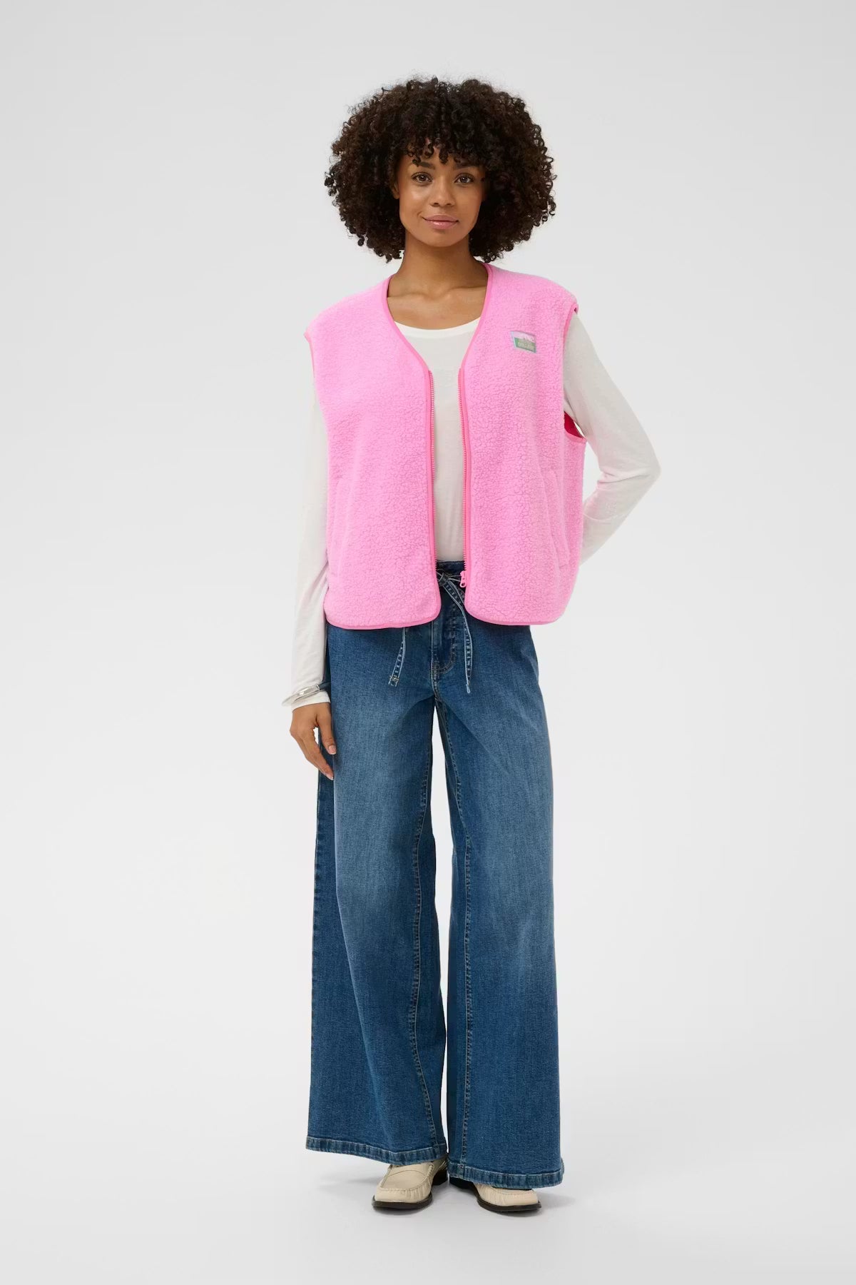 Person wearing a pink vest and blue jeans on a white background