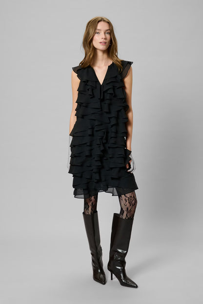 Woman wearing a black ruffled dress and black boots on a gray background