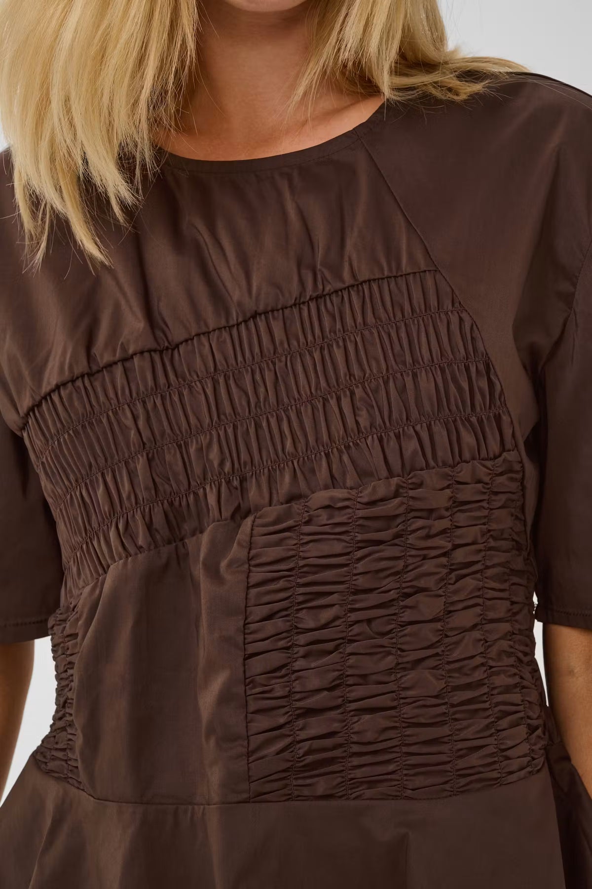 Close-up of a brown short-sleeve dress with a smocked bodice panel and gathered skirt, shown on a model.