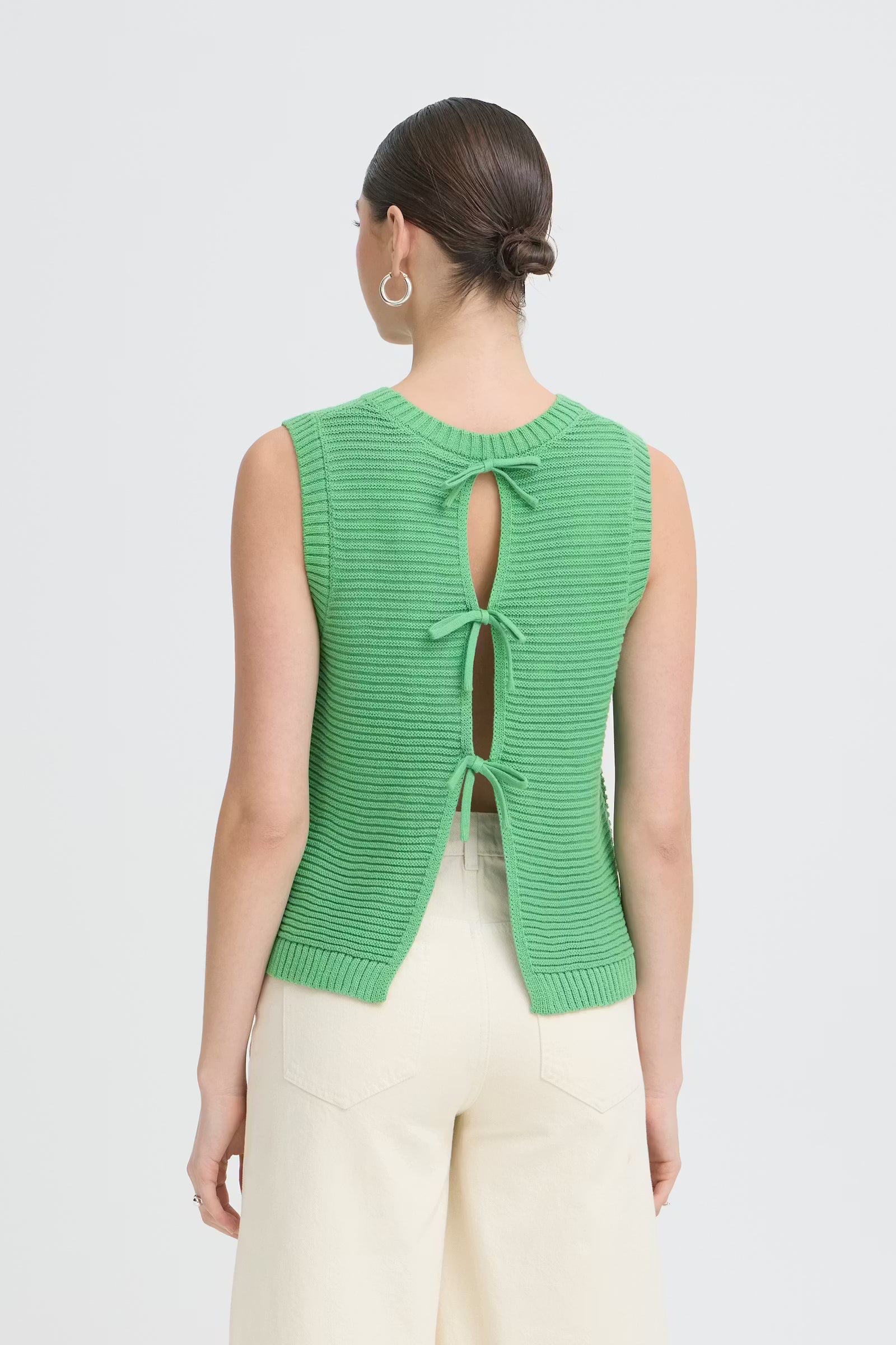 Green knitted vest with open back worn by a person on a light gray background