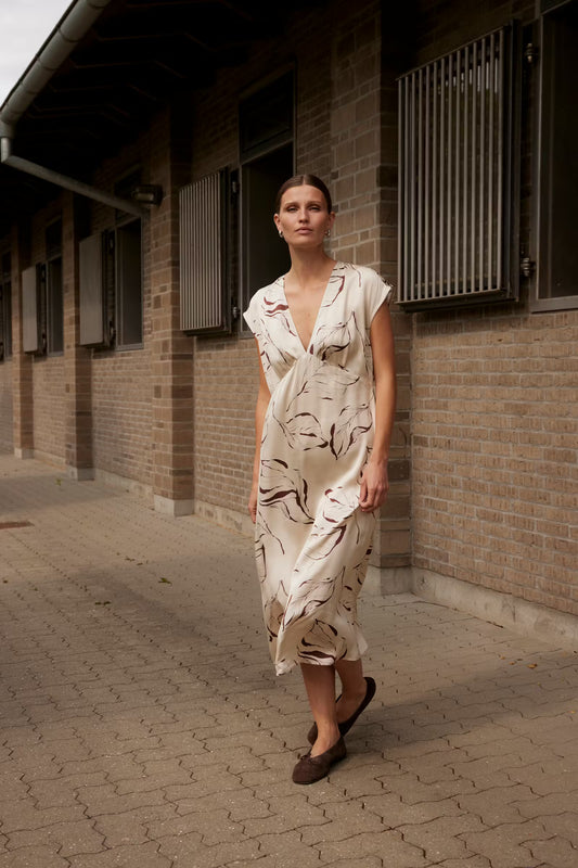 Woman in a patterned dress standing on a brick pavement against a brick wall.