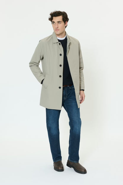 Man wearing a beige coat, black shirt, blue jeans, and brown shoes on a white background