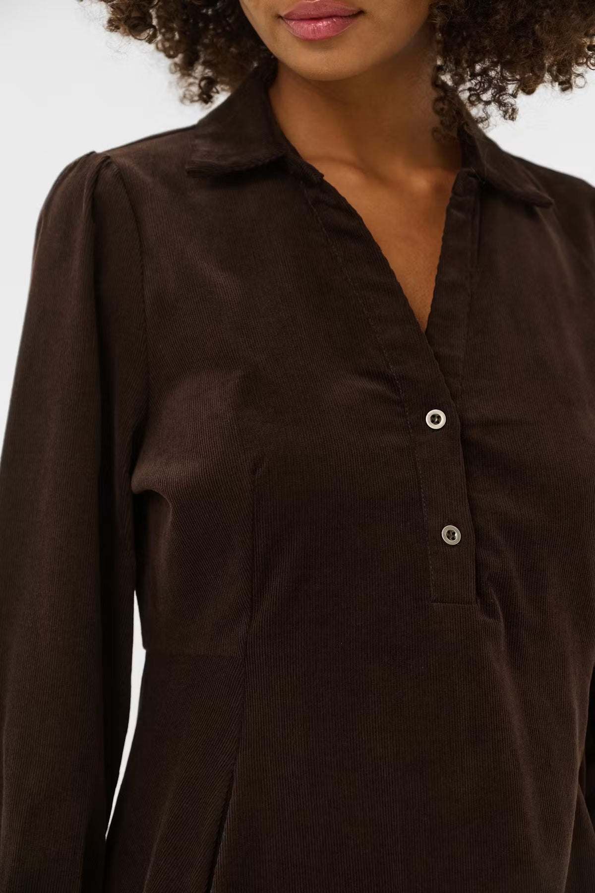 A close-up of a woman wearing a dark brown long-sleeve button-up shirt with a pointed collar and silver buttons.