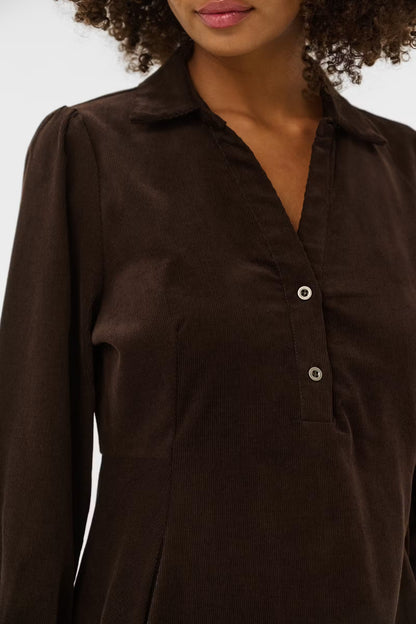 A close-up of a woman wearing a dark brown long-sleeve button-up shirt with a pointed collar and silver buttons.